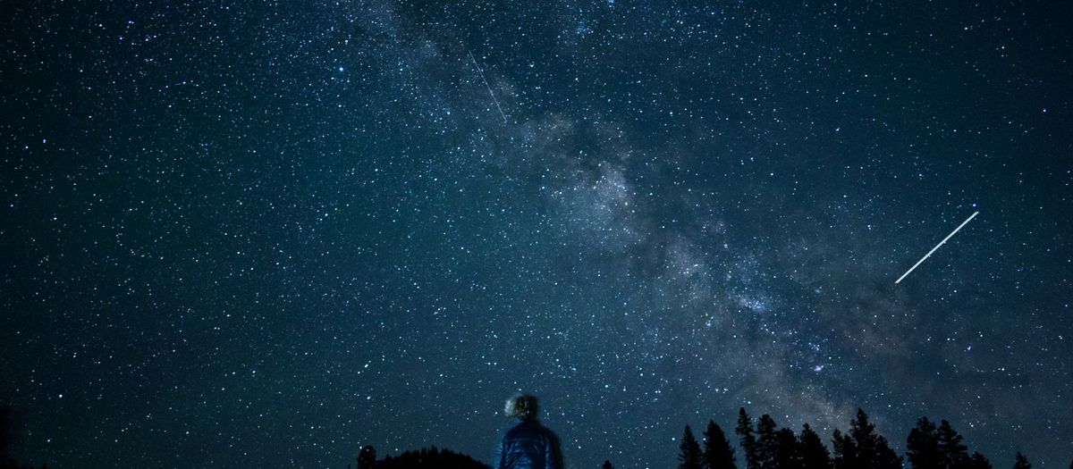 A stargazer standing under a clear night sky on a hillside away from town lights.