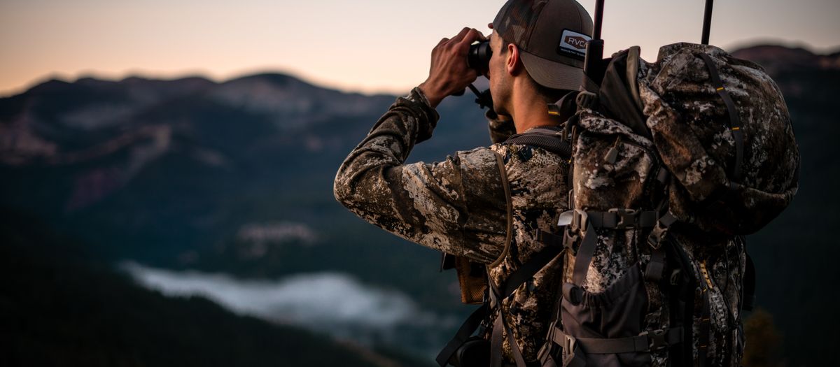 Small compact binoculars clipped to a day pack on a sunlit hiking trail.