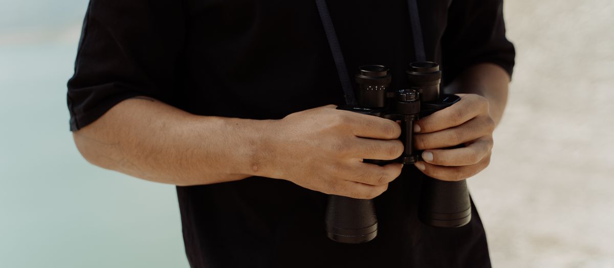 A pair of binoculars resting on a railing at a backyard feeder in soft morning light.