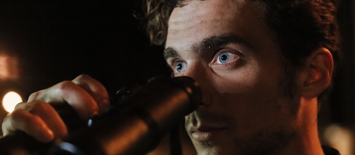 Close-up of a man with intense gaze using binoculars during night time observation.