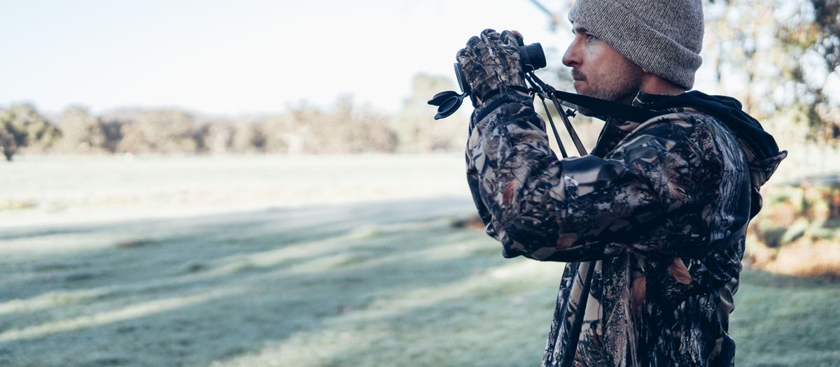 Adult male in camouflage outfit using binoculars in an open field, showcasing outdoor exploration and observation.
